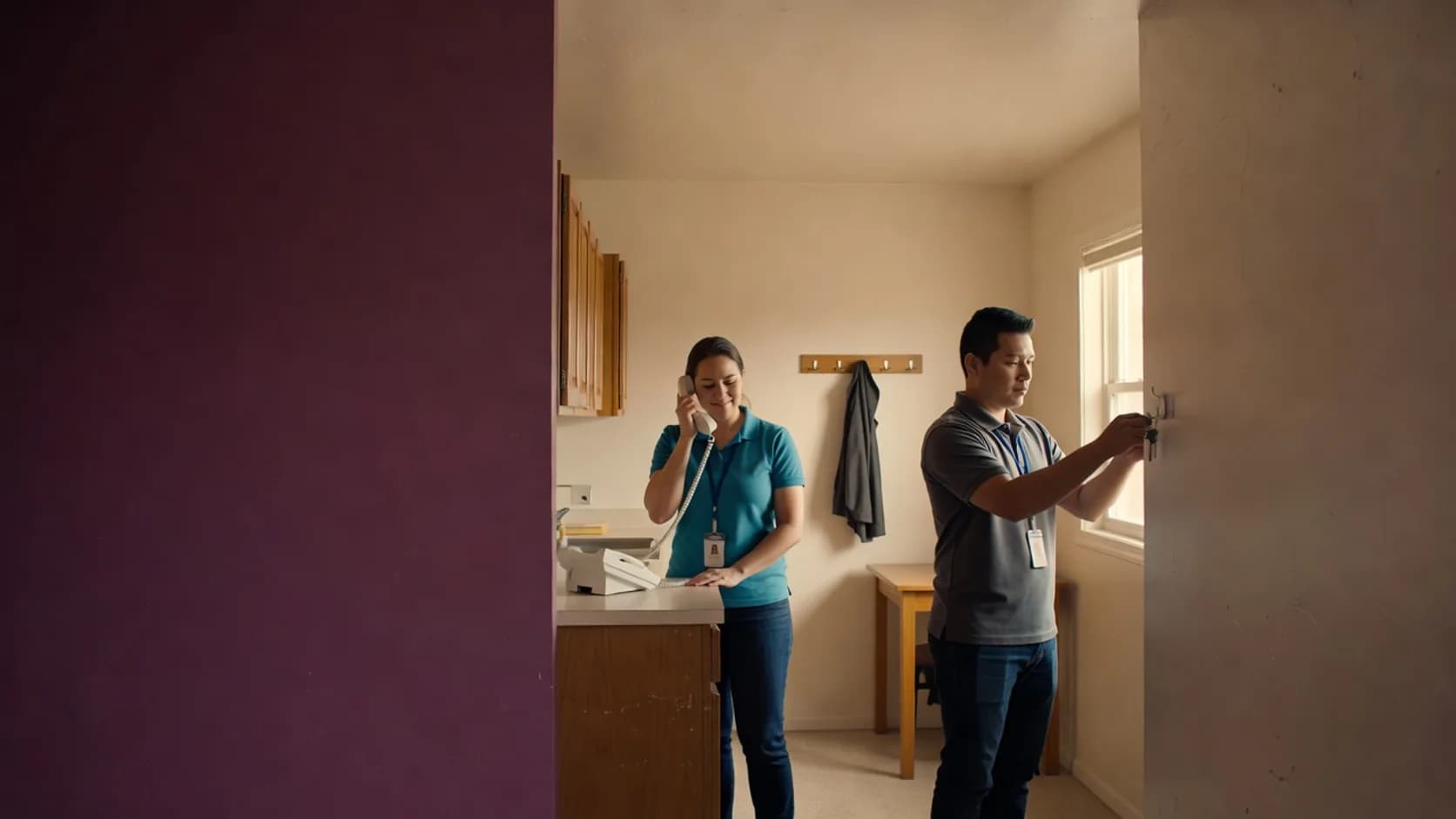 Two group home employees during a shift change, one on the house phone and one hanging up the keys